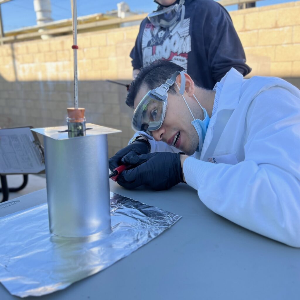 Focused teacher in safety goggles and lab coat conducting an outdoor experiment with equipment on a table.